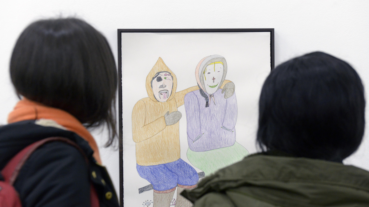 Two people face a pastel drawing of two inuit people.