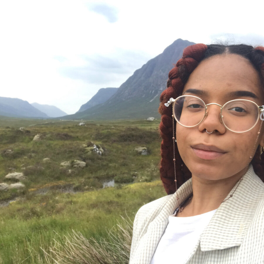 Natasha Thembiso Ruwona wears a white shirt and coat. Mountains and houses are in the background.