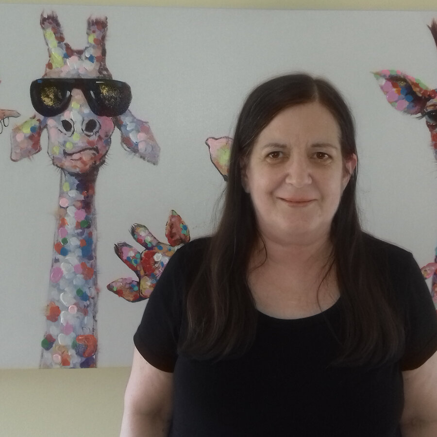 Alison Mackay wears a black t-shirt and stands in front of a painting of three colourful giraffes.